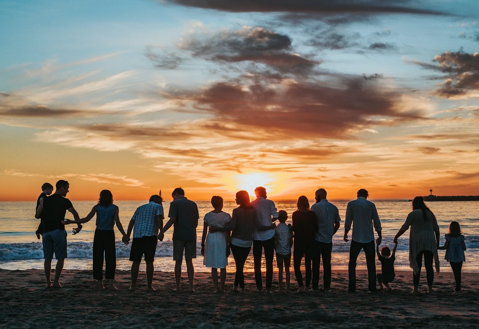 Three generations of a family holding hands together at sunset on the beach